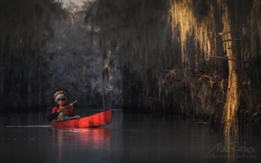 Kayaker-wearing-Native-American-Headdress-paddling-in-the-Bald-Cypress-Trees-alley.-Government-Ditch,-Lake-Caddo,-Texas,-US